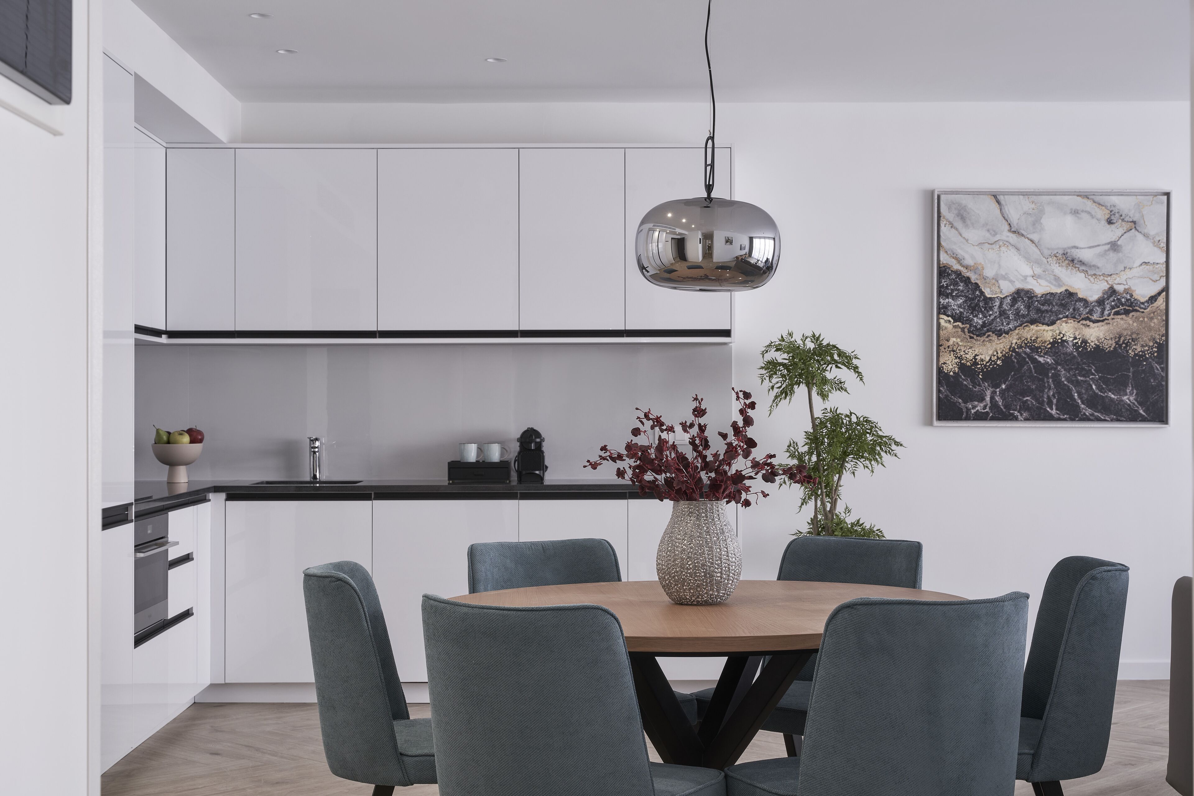 Una cocina moderna con armarios blancos, encimera negra y una lámpara colgante.