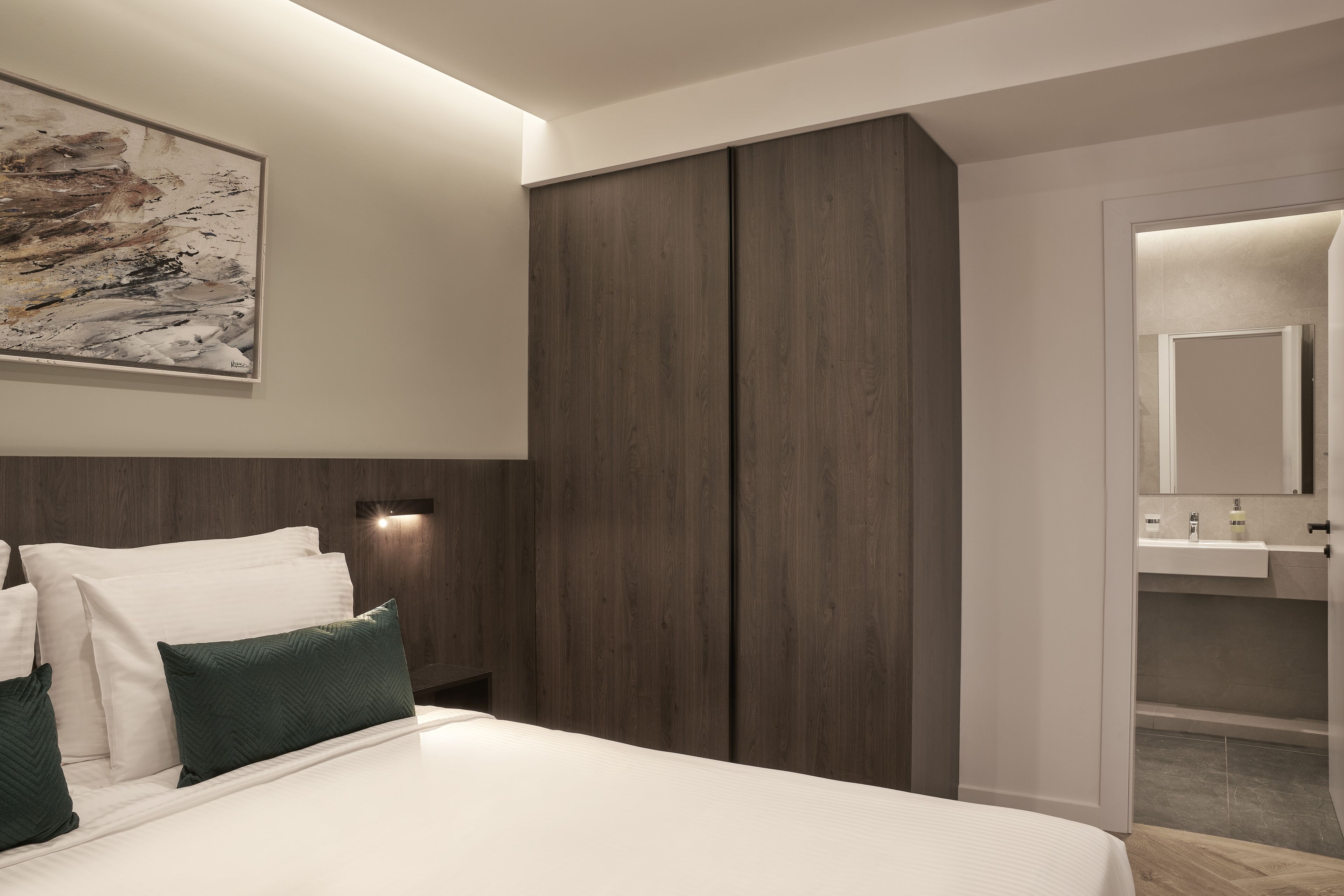 A modern bedroom with a large bed, dark wood wardrobe, and a wall-mounted artwork.