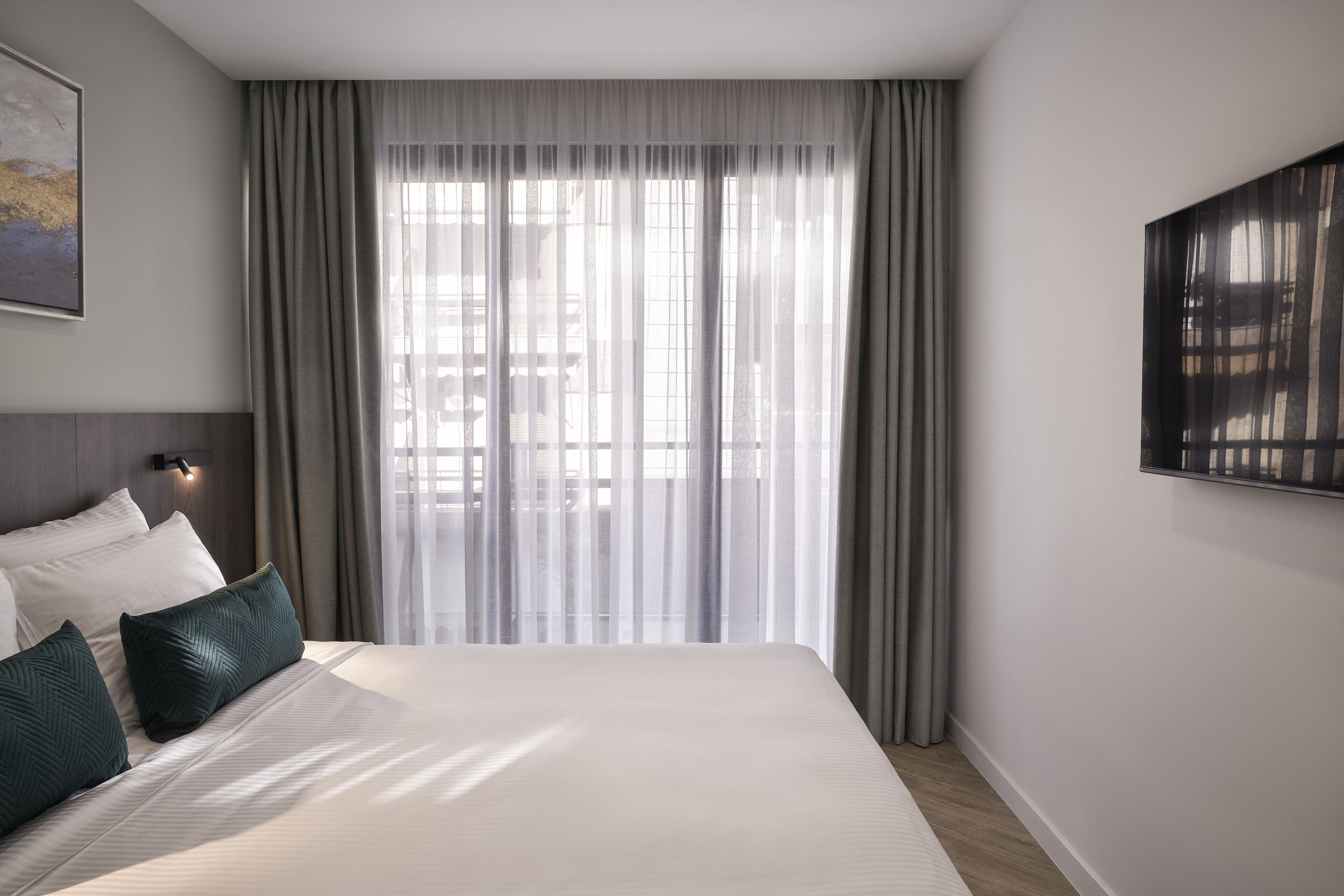 Une chambre d’hôtel avec un grand lit, des rideaux gris, une lampe fixée au mur et un tableau.