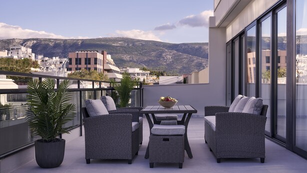A modern balcony with wicker furniture, a table with a fruit bowl, and a view of the city and mountains. - Hestia - Dimitressa 4 (Athens)