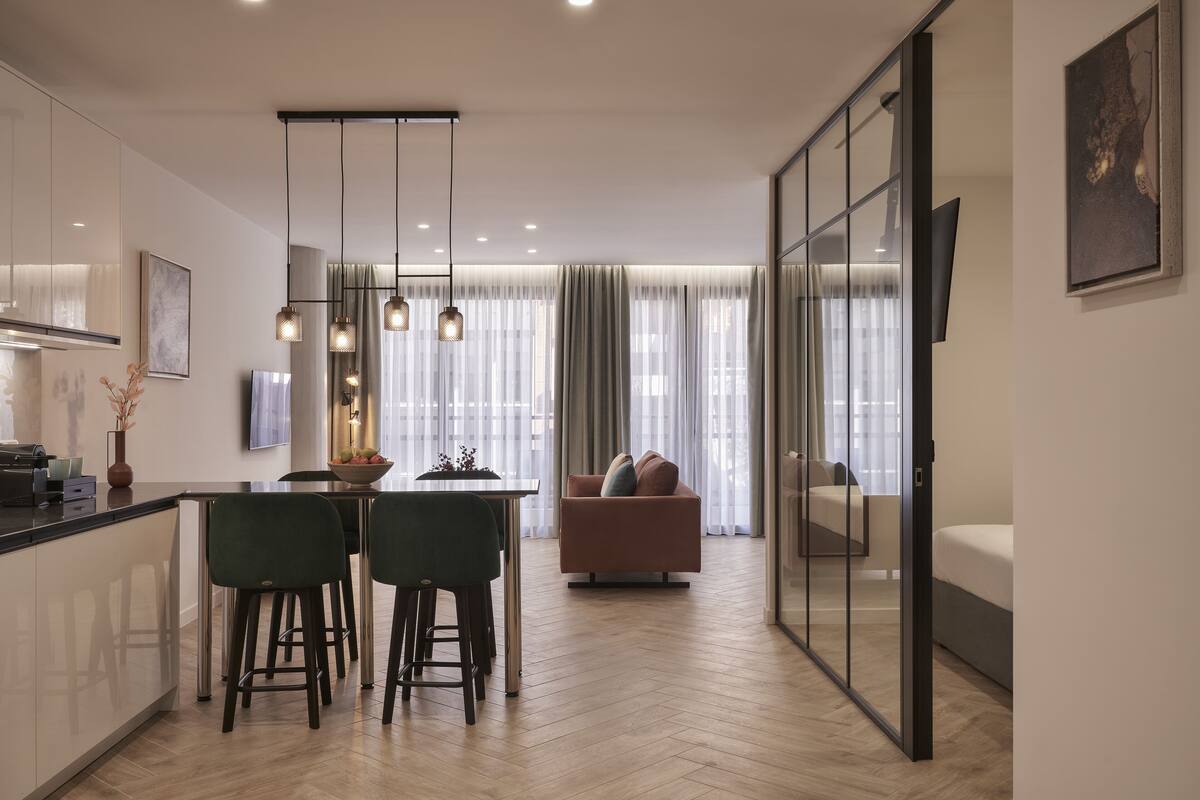 A modern kitchen with a dining area, a sofa, and a glass partition.