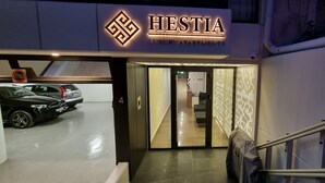 A luxury apartment entrance with a sign reading "HESTIA LUXURY APARTMENTS," a covered parking area, and a staircase leading inside. - Hestia - Dimitressa 4 (Athens)