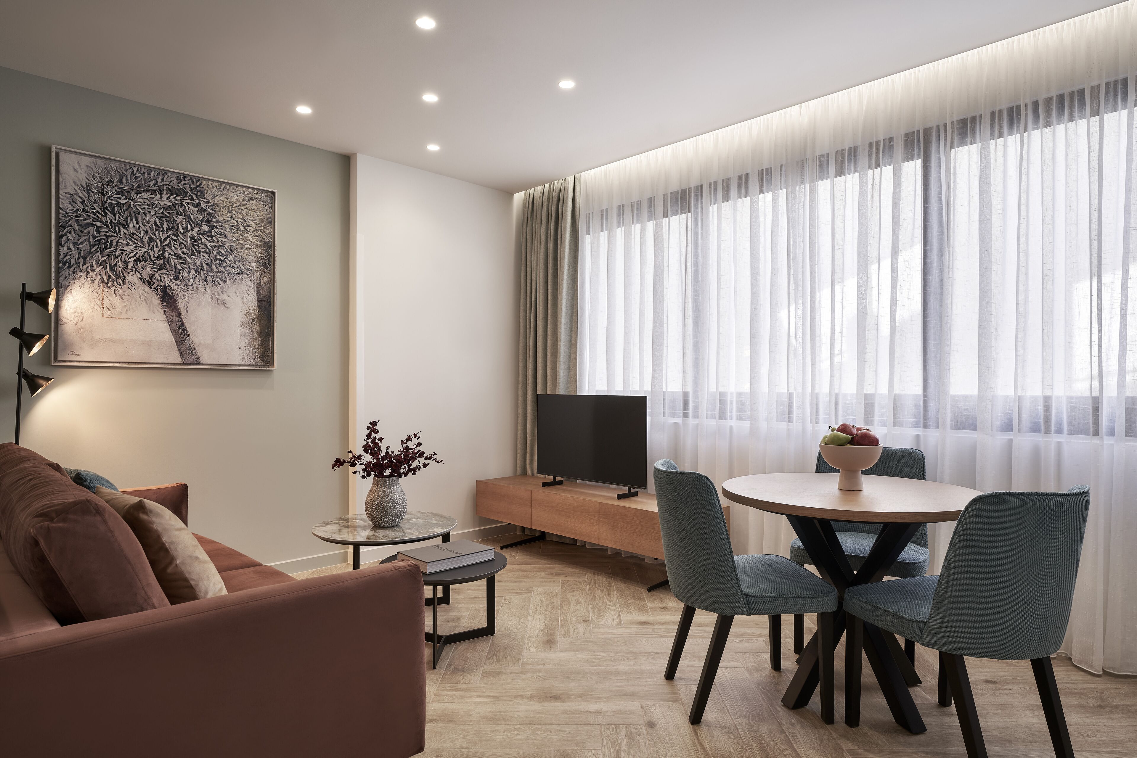 A modern living room with a sofa, a coffee table, a TV on a wooden console, and a dining area with chairs and a table.