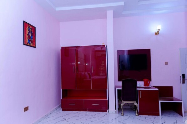 A room with a red wardrobe, a desk with a chair, and a TV.