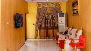 Une chambre d’hôtel avec un lustre, un canapé, un fauteuil rouge et une fenêtre avec des rideaux.