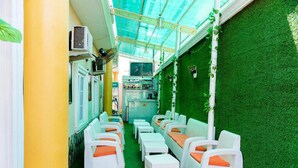 Un petit espace extérieur aménagé en coin salon, à l’abri, avec des meubles en osier blanc et un gazon artificiel vert.