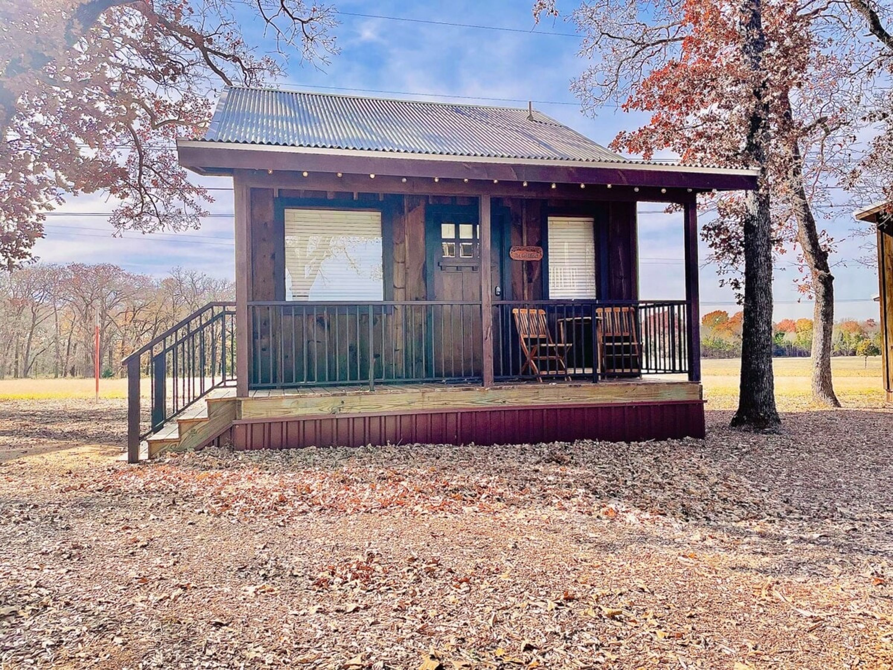 A small cabin with a porch, a wooden deck, and a metal roof.