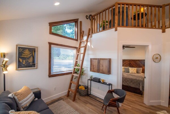 Una sala de estar acogedora con una escalera de madera, un sofá, un escritorio y una cama en la habitación contigua.
