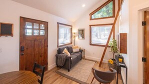A cozy living room with a wooden door, a sofa, a dining table, and a staircase.