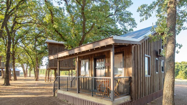 A wooden cabin with a porch, surrounded by trees.