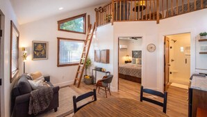 A spacious living area with a loft bedroom, wooden staircase, and a view of the outdoors.