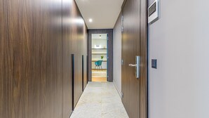 Un couloir avec des portes en bois, un sol carrelé et une vue sur une pièce où se trouvent une chaise et un bureau.