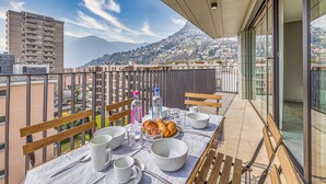 Un balcon avec une table préparée pour le petit-déjeuner, comprenant du pain, des tasses et des bouteilles.