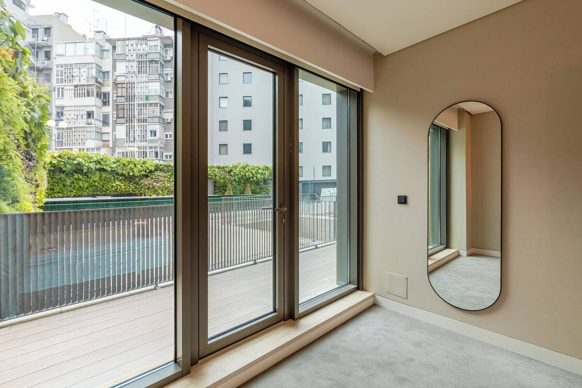 A modern apartment with large sliding glass doors leading to a balcony, a round mirror on the wall, and a view of a residential building.