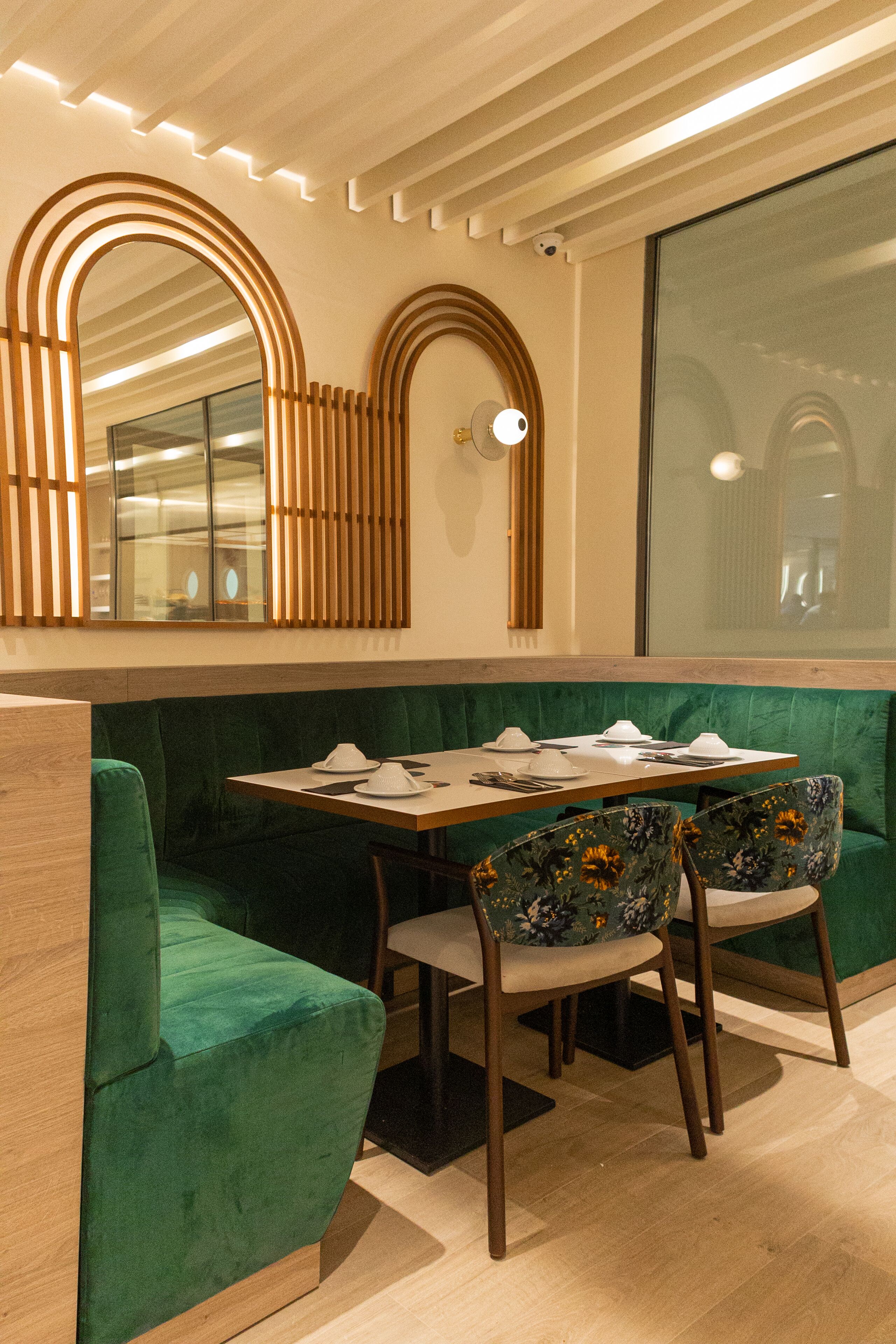 A dining area with a green cushioned bench, a wooden table set with plates and cutlery, and two floral-patterned chairs.