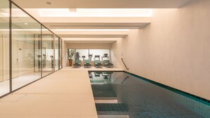 A modern indoor swimming pool with clear glass walls, a tiled floor, and a ceiling with recessed lighting. - Luster Hotel (Lisbon)