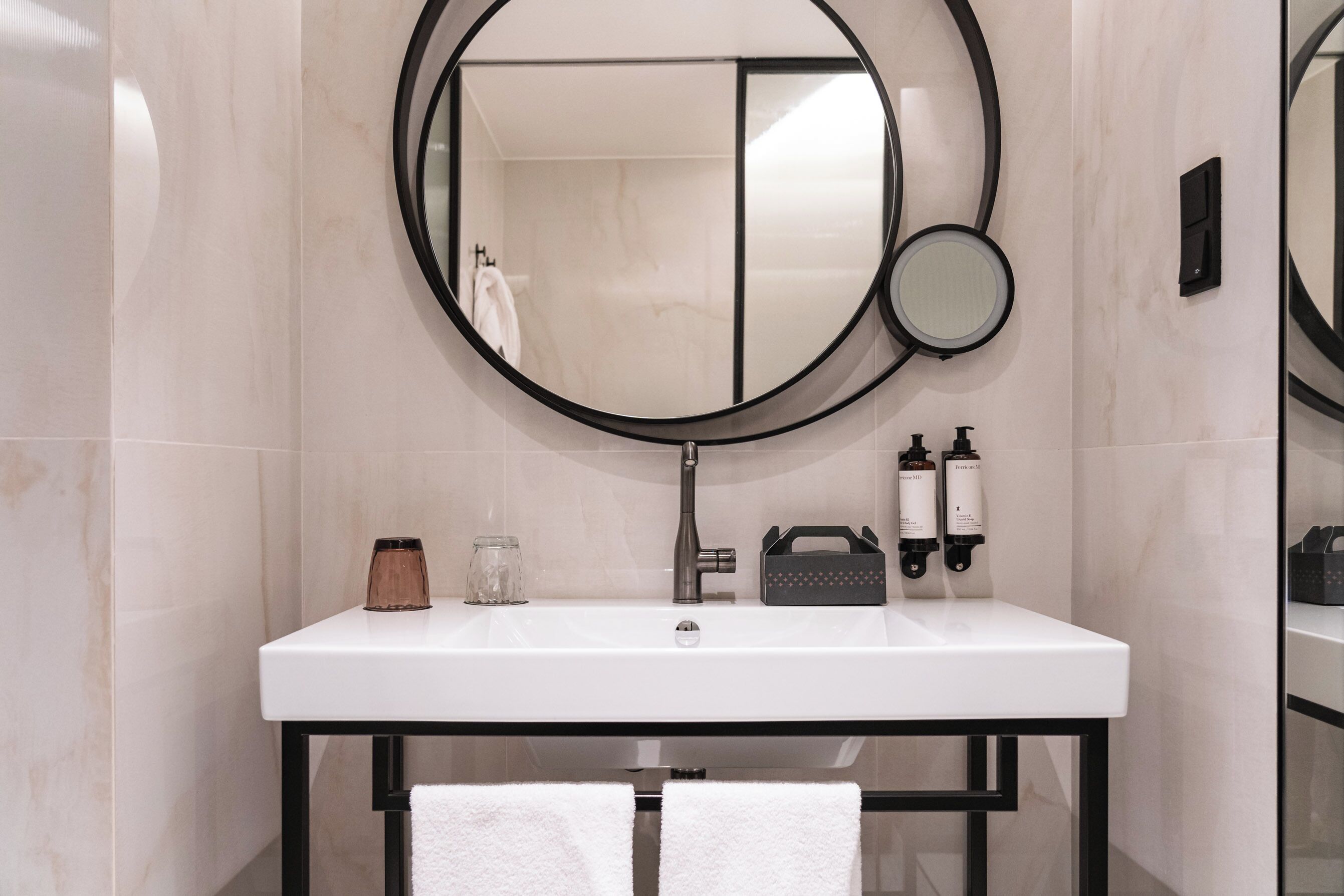 Een badkamer met een wit wastafel, een ronde spiegel, een handdoekhouder en toiletartikelen.
