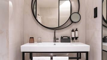 Een badkamer met een wit wastafel, een ronde spiegel, een handdoekhouder en toiletartikelen.