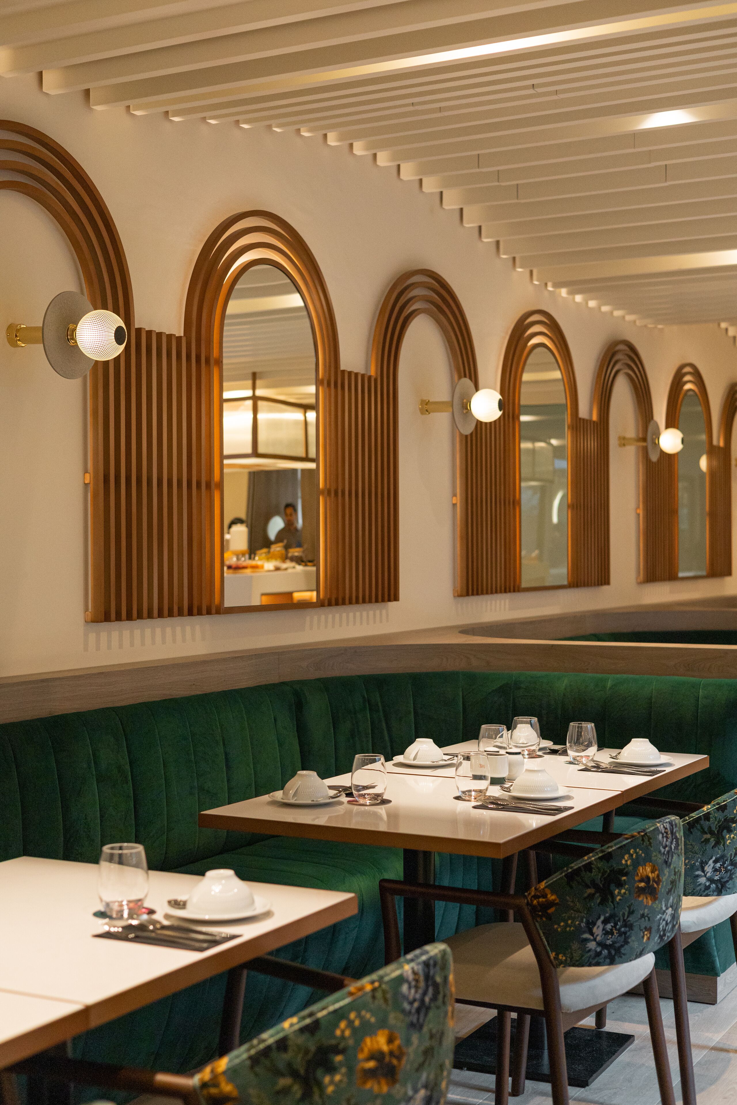 A restaurant with a green upholstered booth seating area, wooden tables, and mirrored wall sconces.