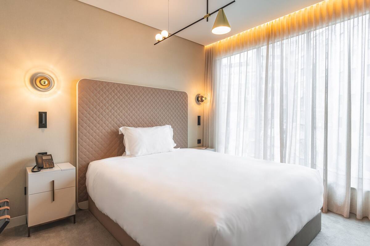 A hotel room with a large bed, a bedside table with a phone, and a window with curtains.