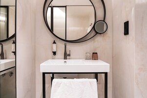 A modern bathroom with a white sink, black faucet, and a round mirror with a smaller mirror below it.