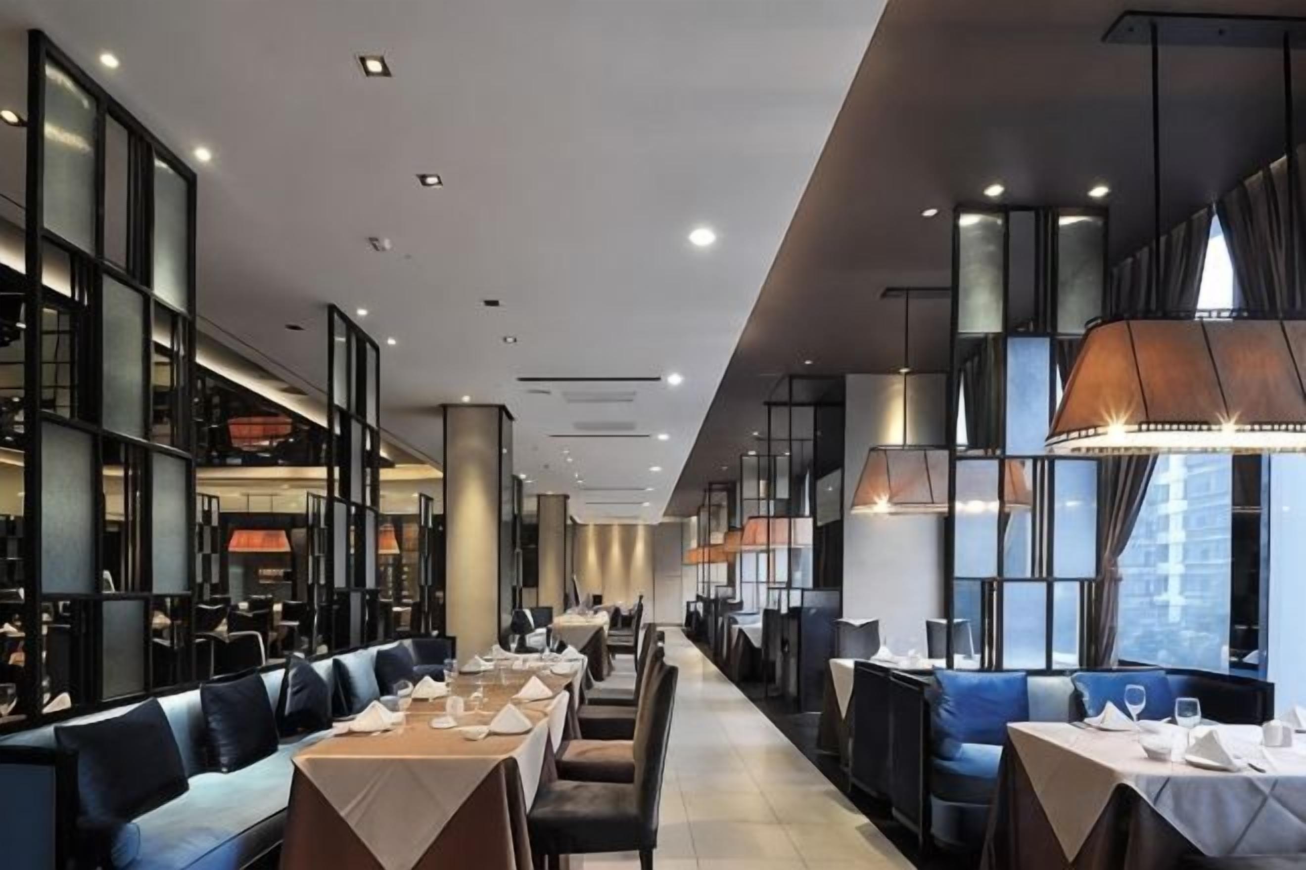Ein modernes Restaurant mit langen Tischen, Sitzgelegenheiten in Boxen, hohen Decken und großen Fenstern.