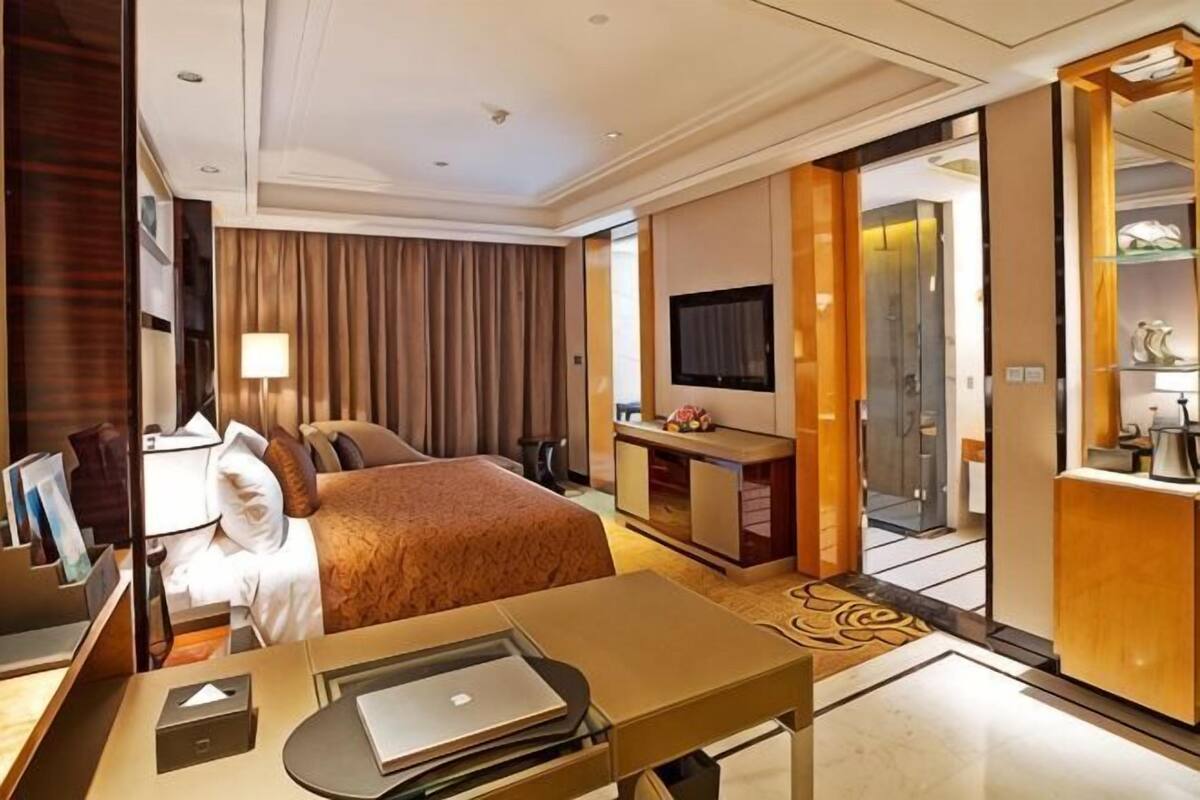 A hotel room with a bed, desk, TV, and a view of the outside.