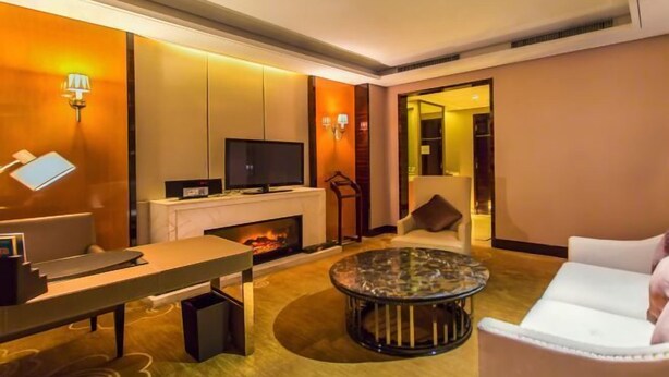 A modern living room with a fireplace, a television, a sofa, a coffee table, and a desk with a computer. - Xindao International Hotel (Yichang)