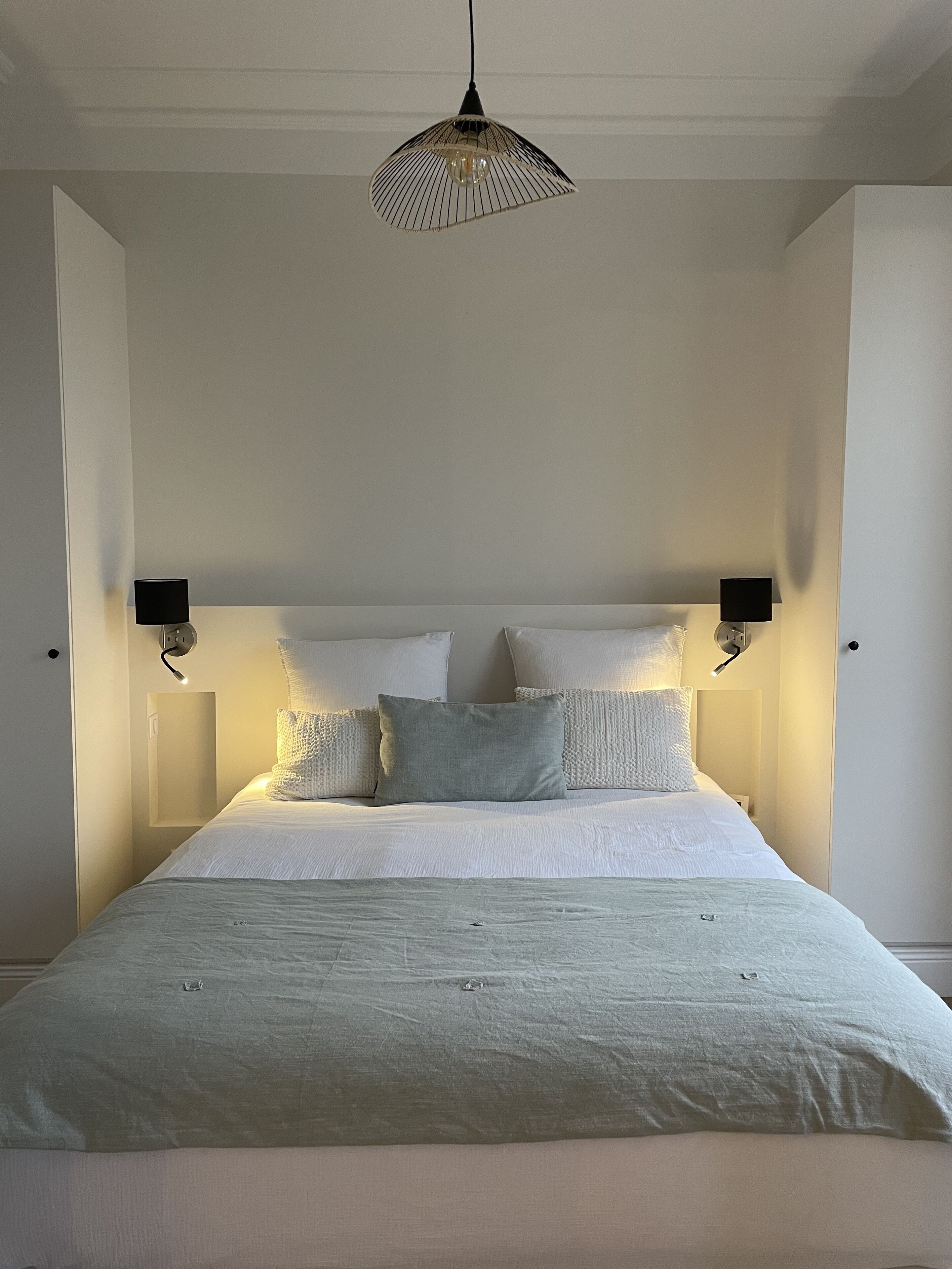 A bedroom with a bed, two wall-mounted lamps, and a hanging light fixture.