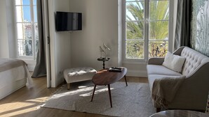 Un soggiorno moderno con divano, tavolino, TV a parete e ampie finestre con vista sulle palme.