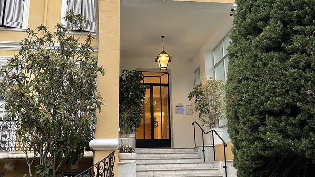 L'ingresso di un hotel con una scalinata che conduce alla porta, circondato da piante in vaso e un grande albero.