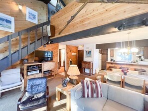 Een gezellige woonkamer met een bank, fauteuil en een televisie. Er is een trap die naar een ander niveau leidt.