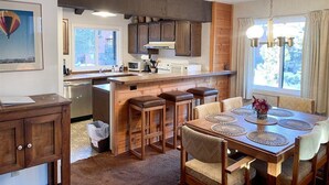 Una cucina con mobili in legno, un'isola centrale con sgabelli, un tavolo da pranzo con sottopiatti e una finestra con tende.