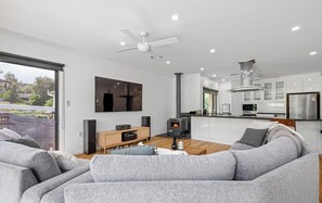 Ein modernes Wohnzimmer mit einer Couch, einem Fernseher, einem Kamin und einer Küchenzeile inklusive Schränke und Geräte.