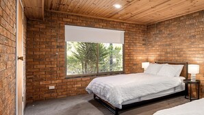 Une chambre avec un mur en briques, une grande fenêtre, un lit et une table de chevet avec une lampe.