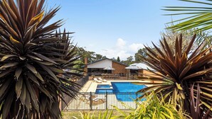 Une piscine entourée de plantes tropicales, avec une maison en arrière-plan.