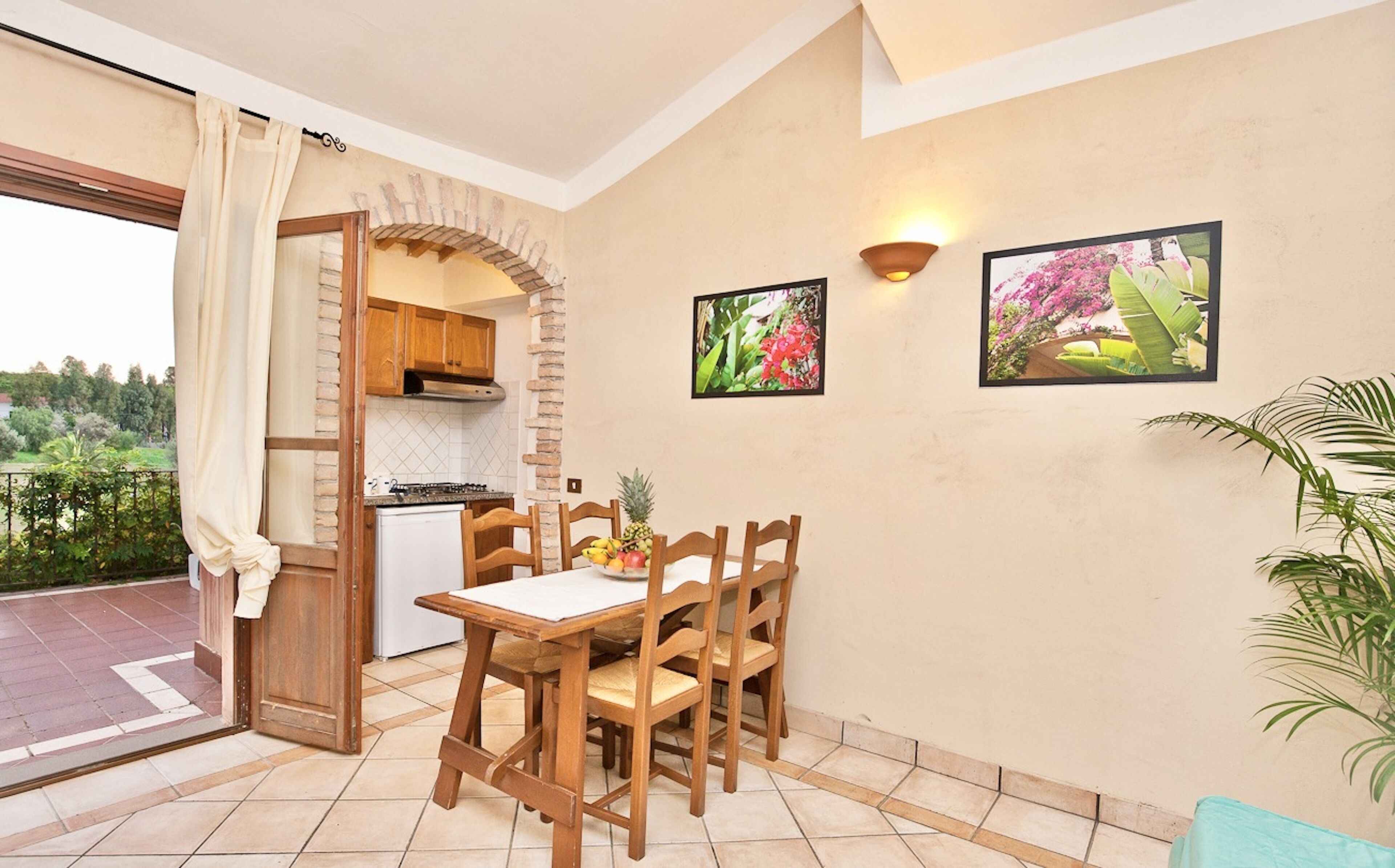 A dining area with a table and chairs, a kitchen in the background, and two framed pictures on the wall.