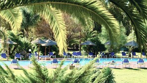 A pool area with lounge chairs and umbrellas, surrounded by palm trees and greenery. - Residence con piscina a 250 mt dal mare  (Pula)