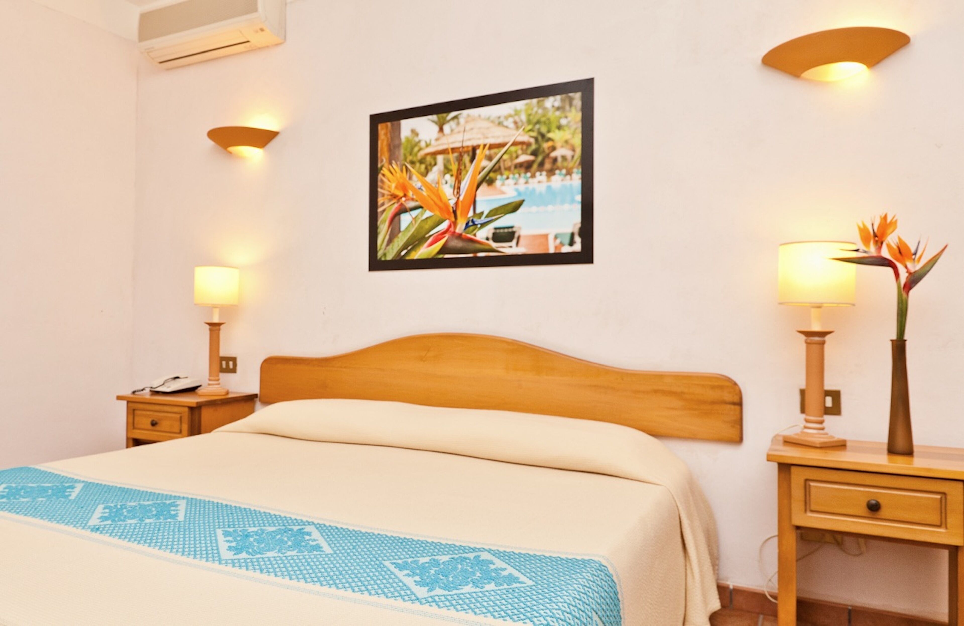 A hotel room with a bed, two bedside tables with lamps, a wall-mounted picture, and a nightstand with a phone.