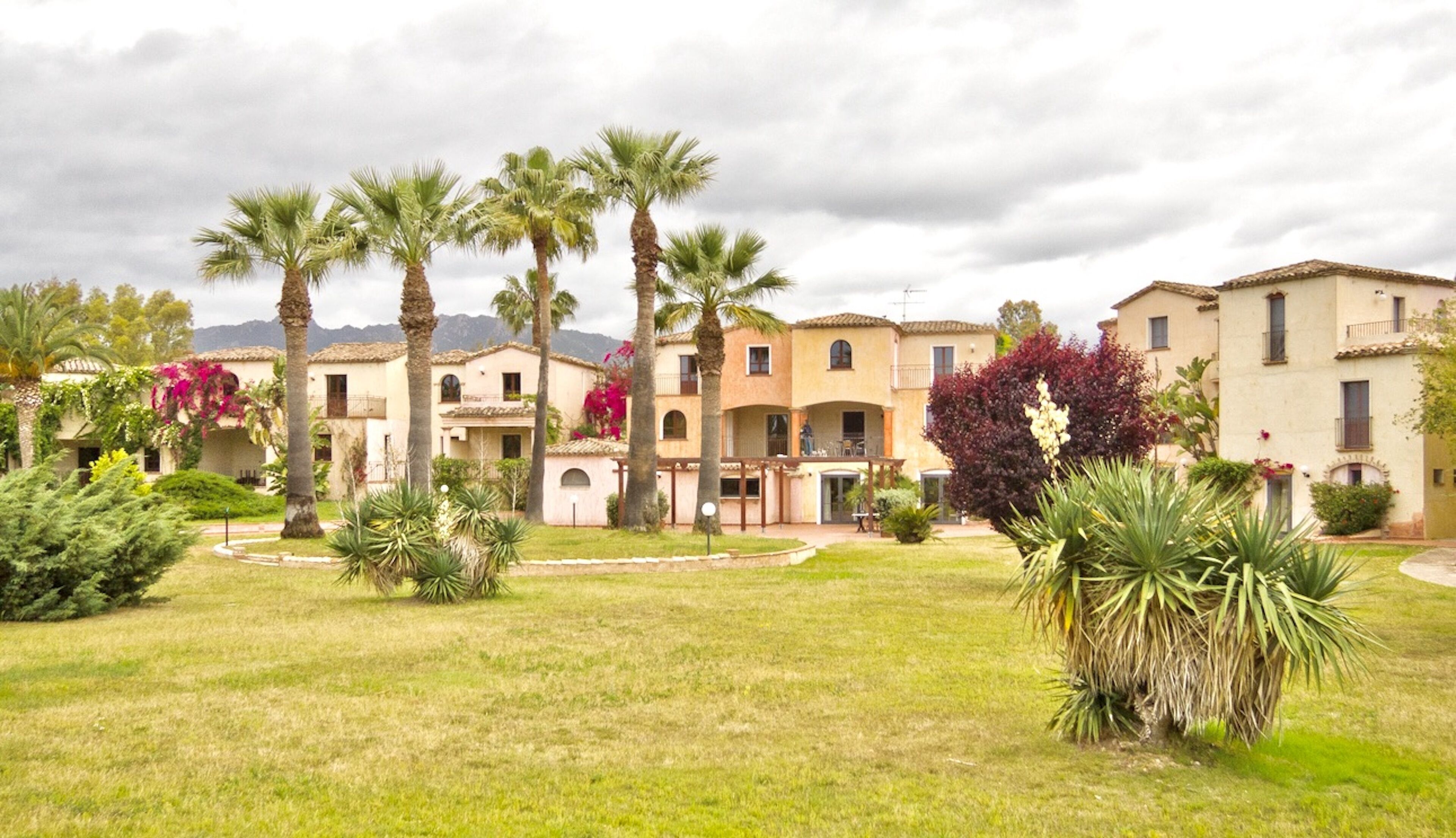 A courtyard with palm trees, a garden, and a row of Mediterranean-style buildings with balconies.