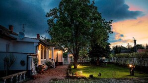 A residential property with a paved driveway, a large tree, and a well-lit house at dusk. - Treasure Of The Past With Whirlpool (Balatonrendes)