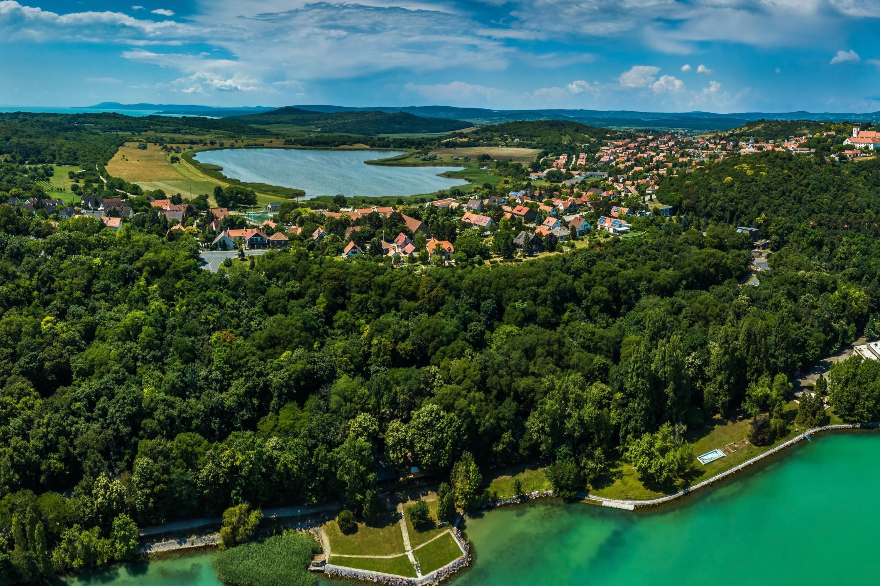 An aerial view of a lakeside town with dense greenery, a clear lake, and a mix of residential and commercial buildings.