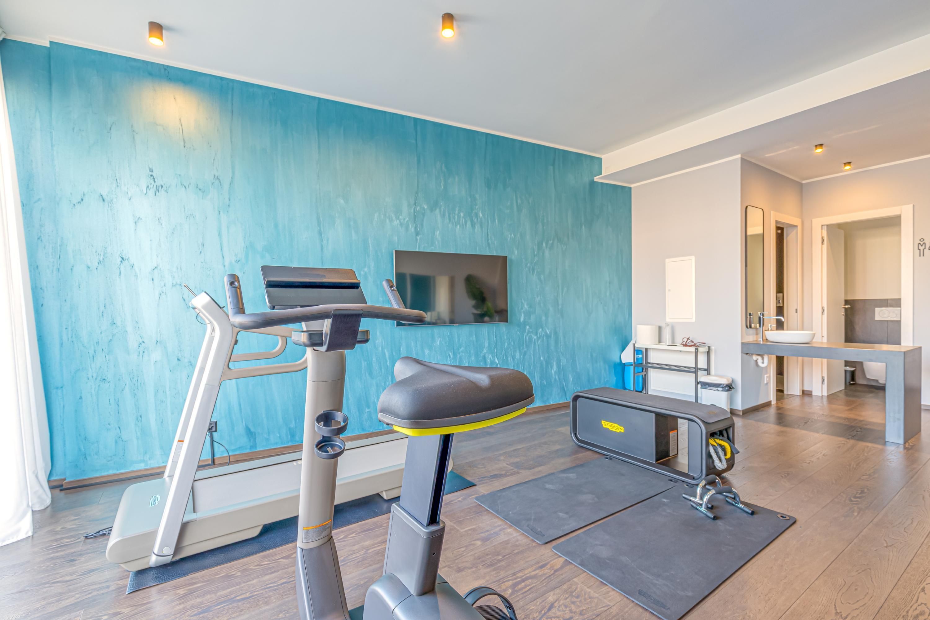 A modern living room with a treadmill, a flat-screen TV, and a dining area.