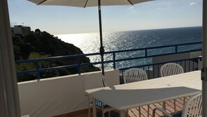 A balcony with a table and chairs, a white umbrella, and a view of the sea.