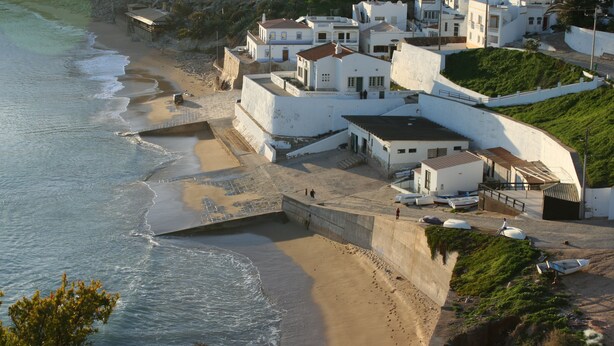 A coastal village with white buildings, a beach, and a rocky hillside.