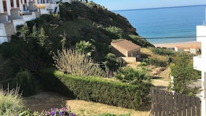 A coastal residential area with a white building, a small house, and a beach in the background.