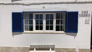 A building facade with a window featuring blue shutters, a tiled bench below, and a sign reading "CASA VALERIA".