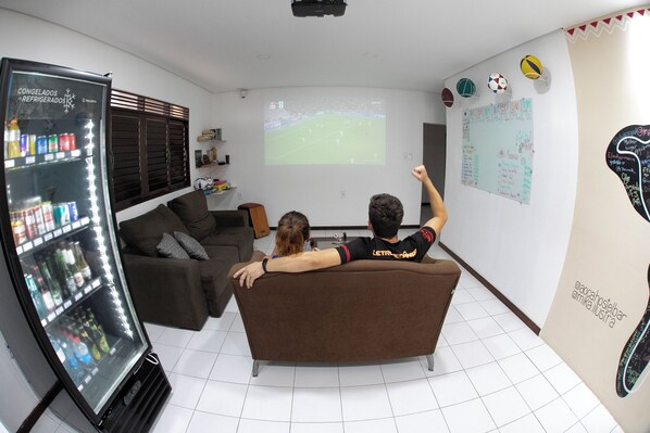 Una sala de estar con una pantalla grande, un refrigerador y un sofá.