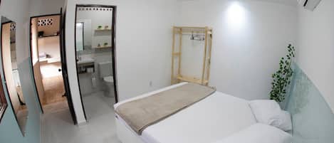 Un dormitorio con una cama, una mesa de madera, un espejo y una planta colgante.