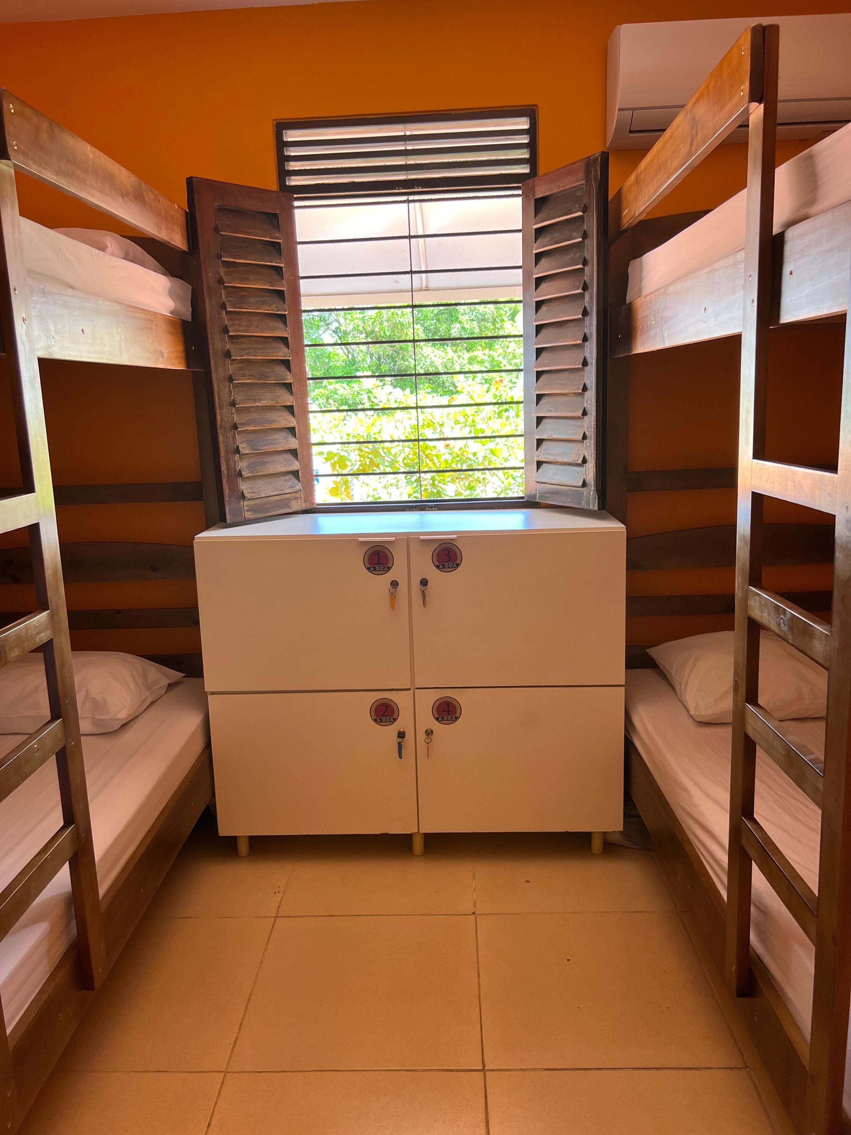 A bunk room with four beds, a window with blinds, and a central storage unit with four compartments.